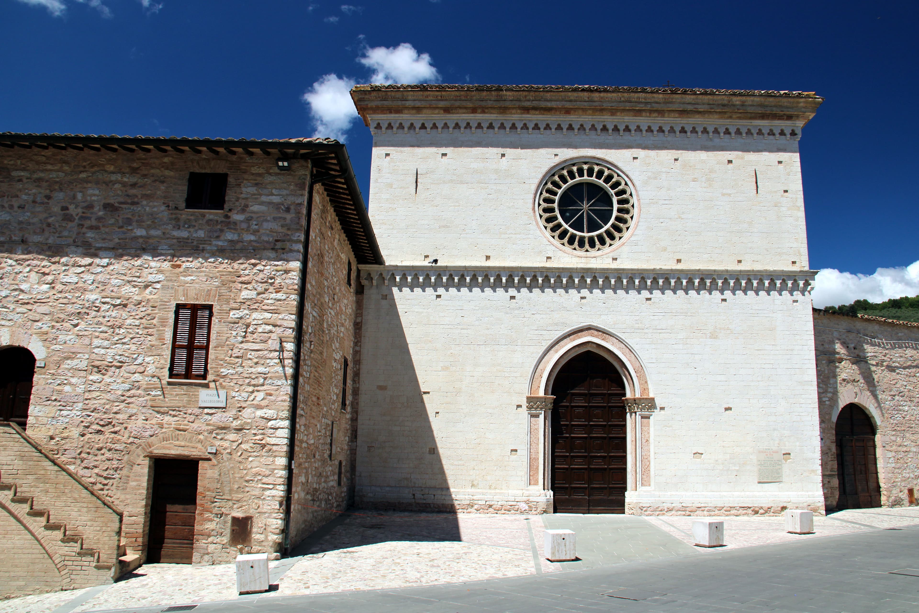 Facciata in pietra chiara della chiesa di Santa Maria di Vallegloria a Spello, con un rosone e il portale ad arco.