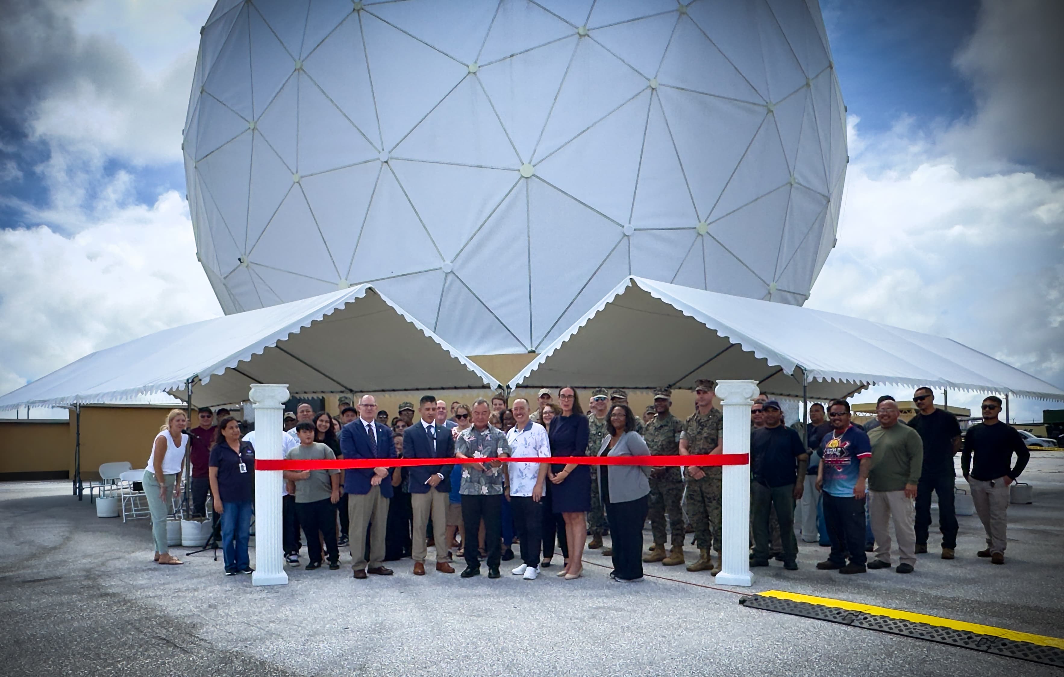 Un gruppo di persone taglia un nastro rosso davanti alla grande cupola bianca dell’antenna della stazione NASA di Guam.