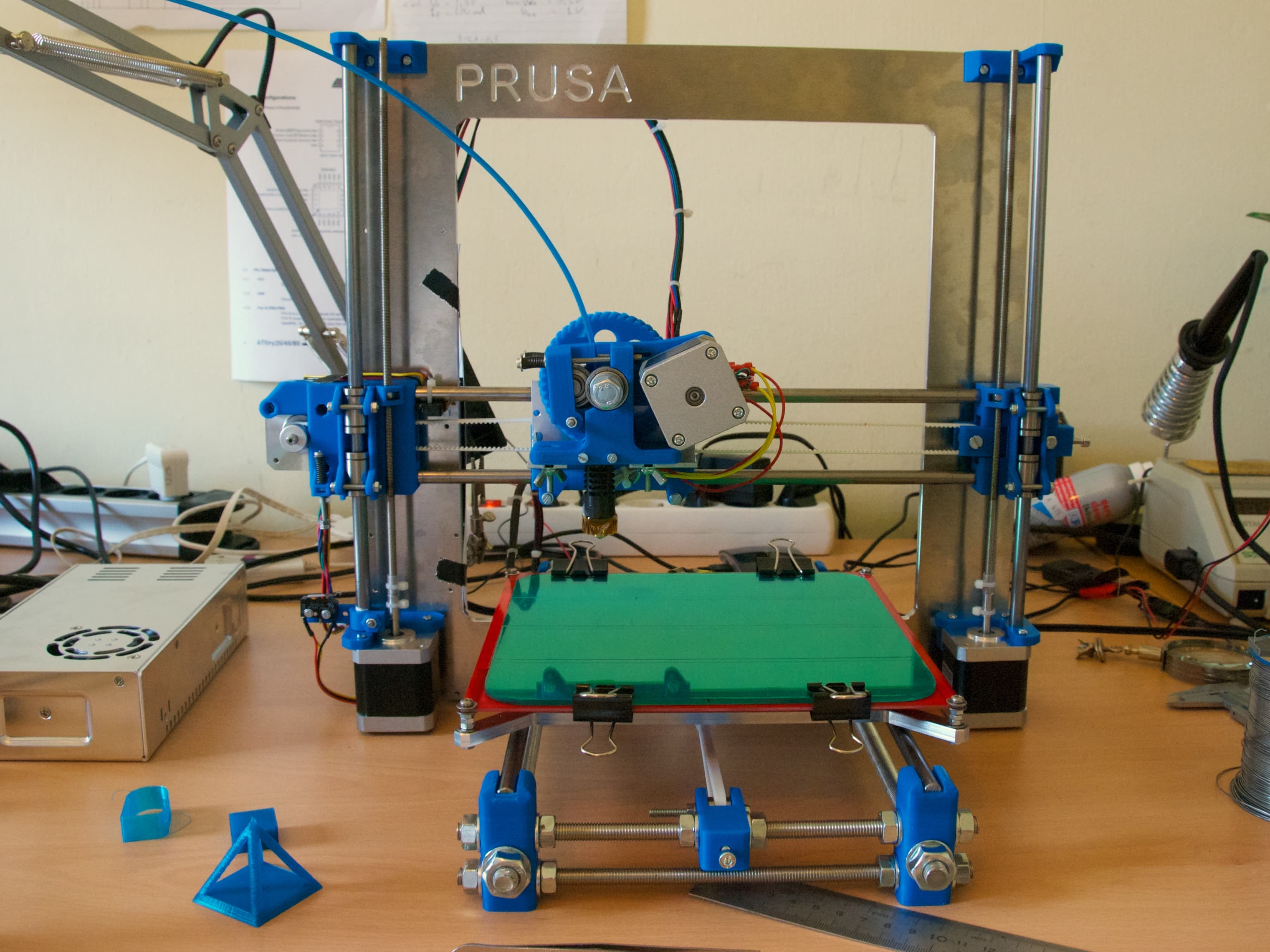 Una stampante 3D Prusa i3 con telaio aperto, cavi e piano di stampa.