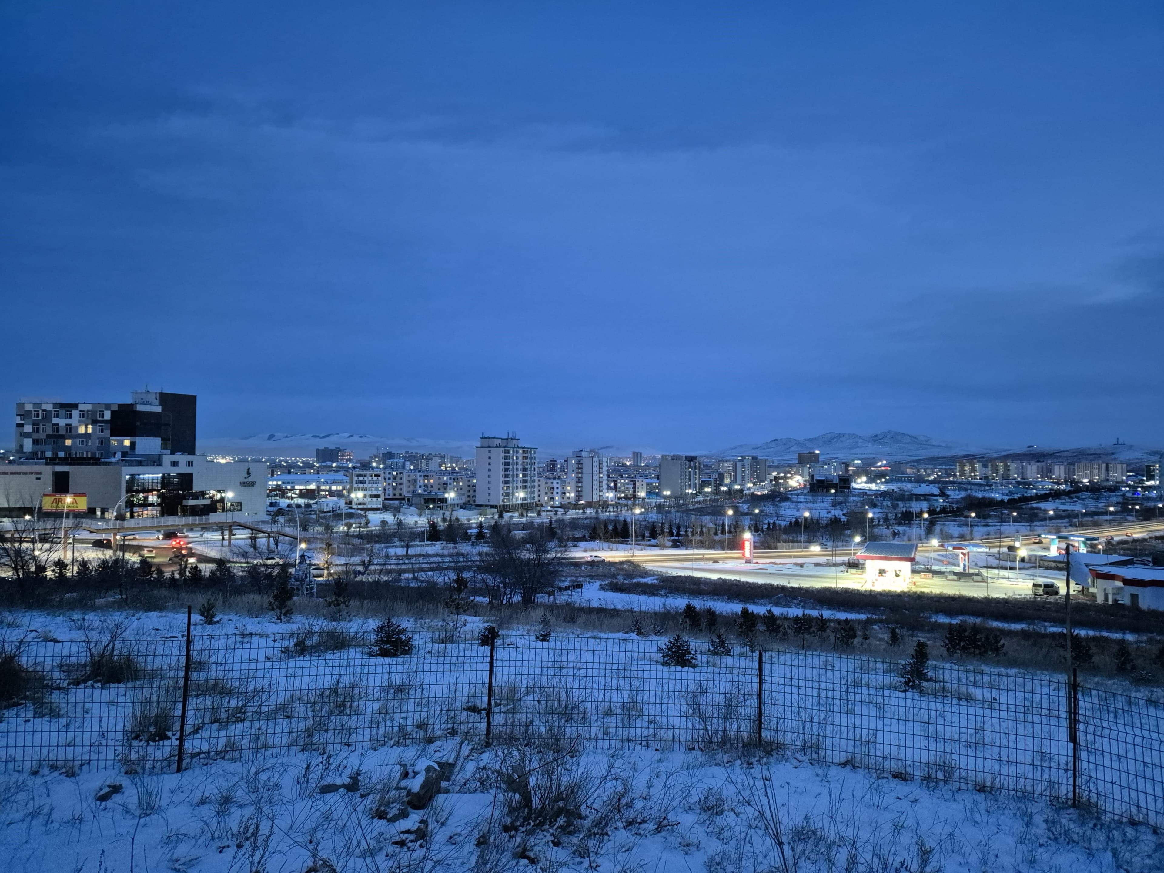 Edifici e strade di Darkhan al crepuscolo, con neve e colline sullo sfondo