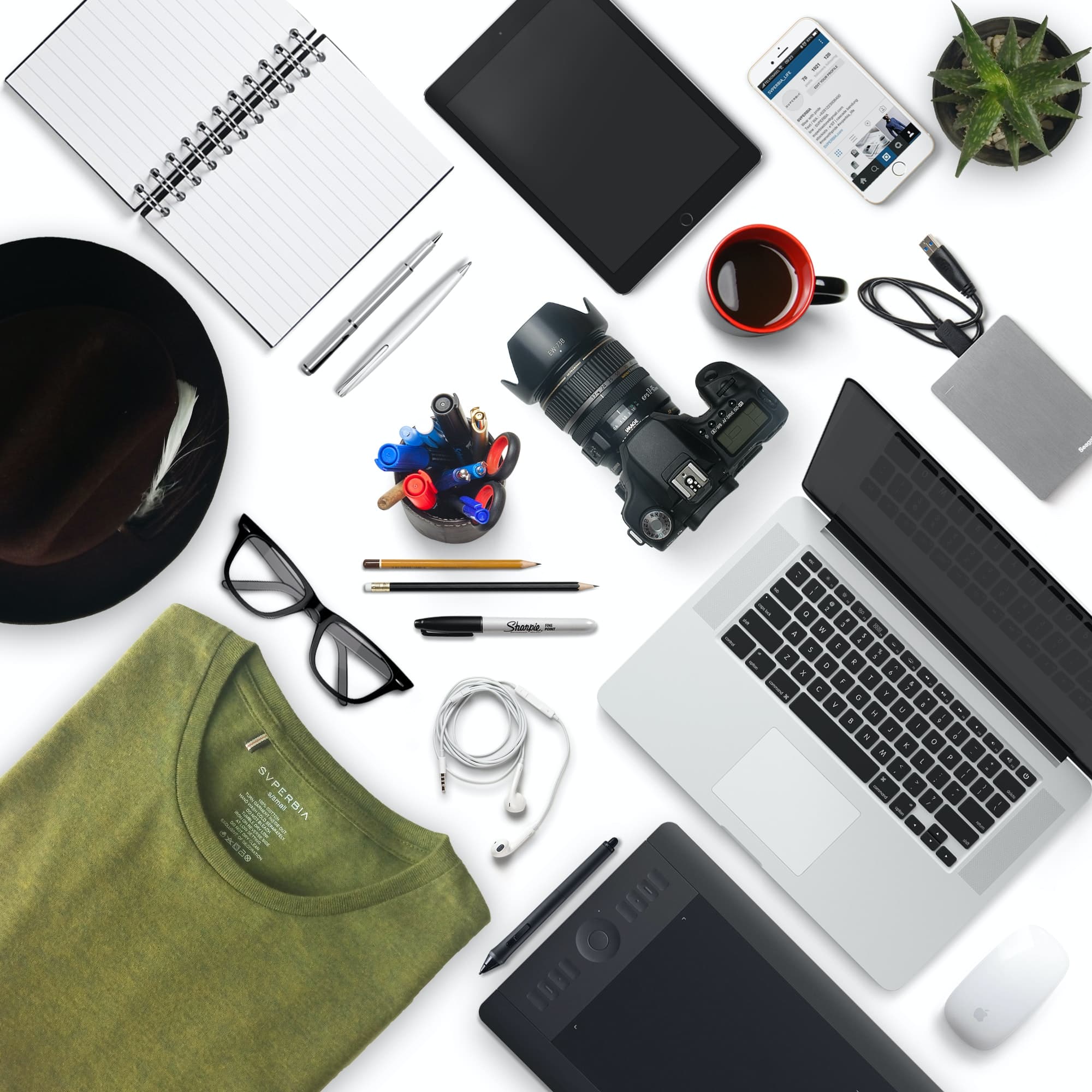 Computer portatile, tablet, quaderno, penne e fotocamera disposti su un tavolo bianco.
