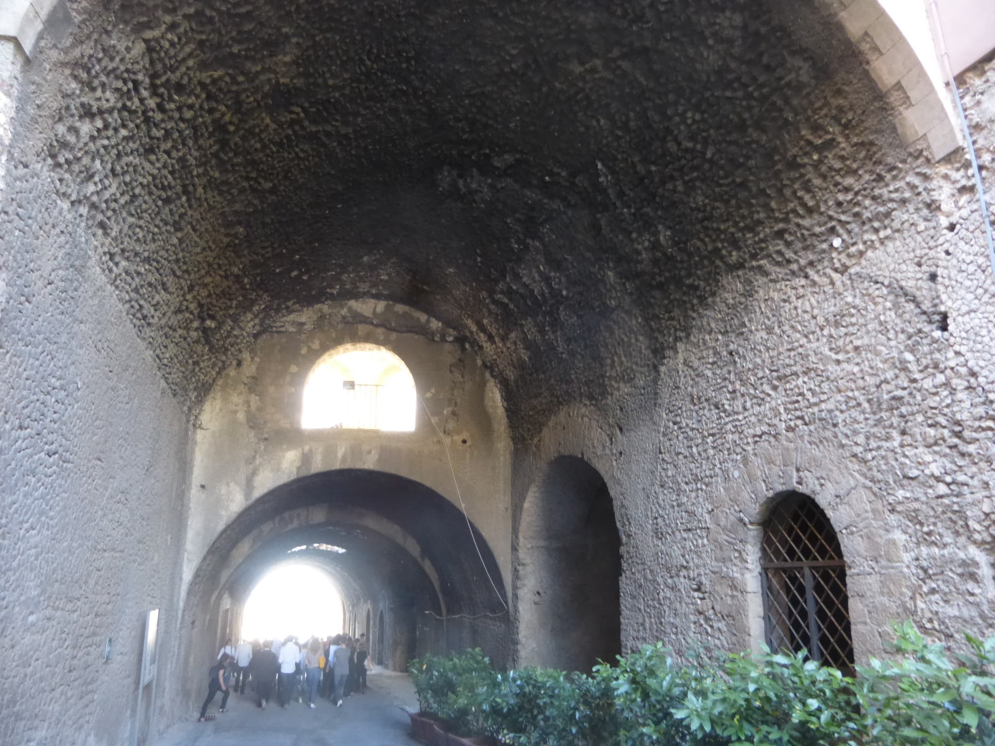 La grande volta e i passaggi in muratura della Via Tecta a Tivoli, con visitatori in fondo e vegetazione lungo un lato.