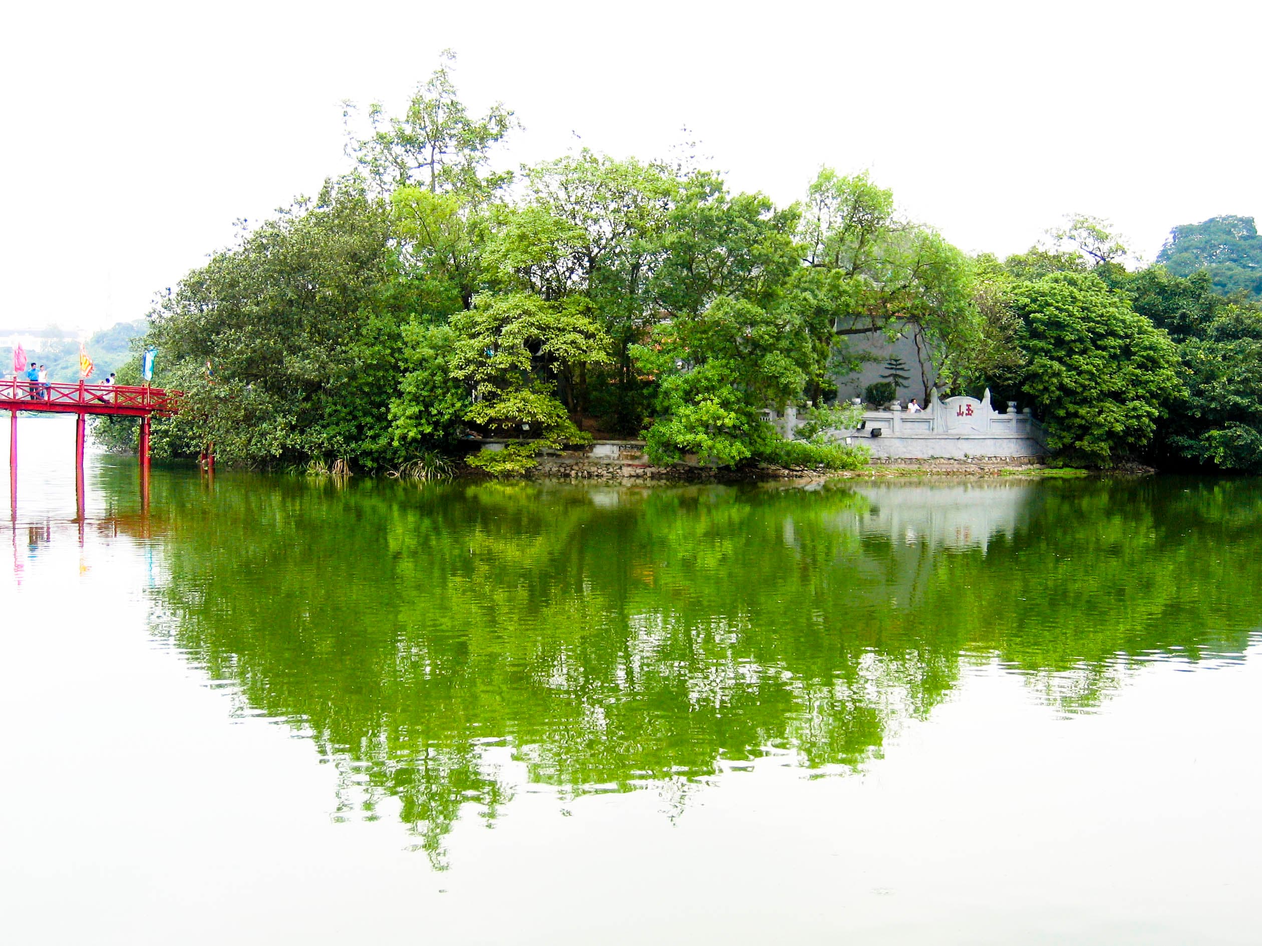 Un ponte rosso e alberi si riflettono nell’acqua del lago Hoan Kiem a Hanoi.