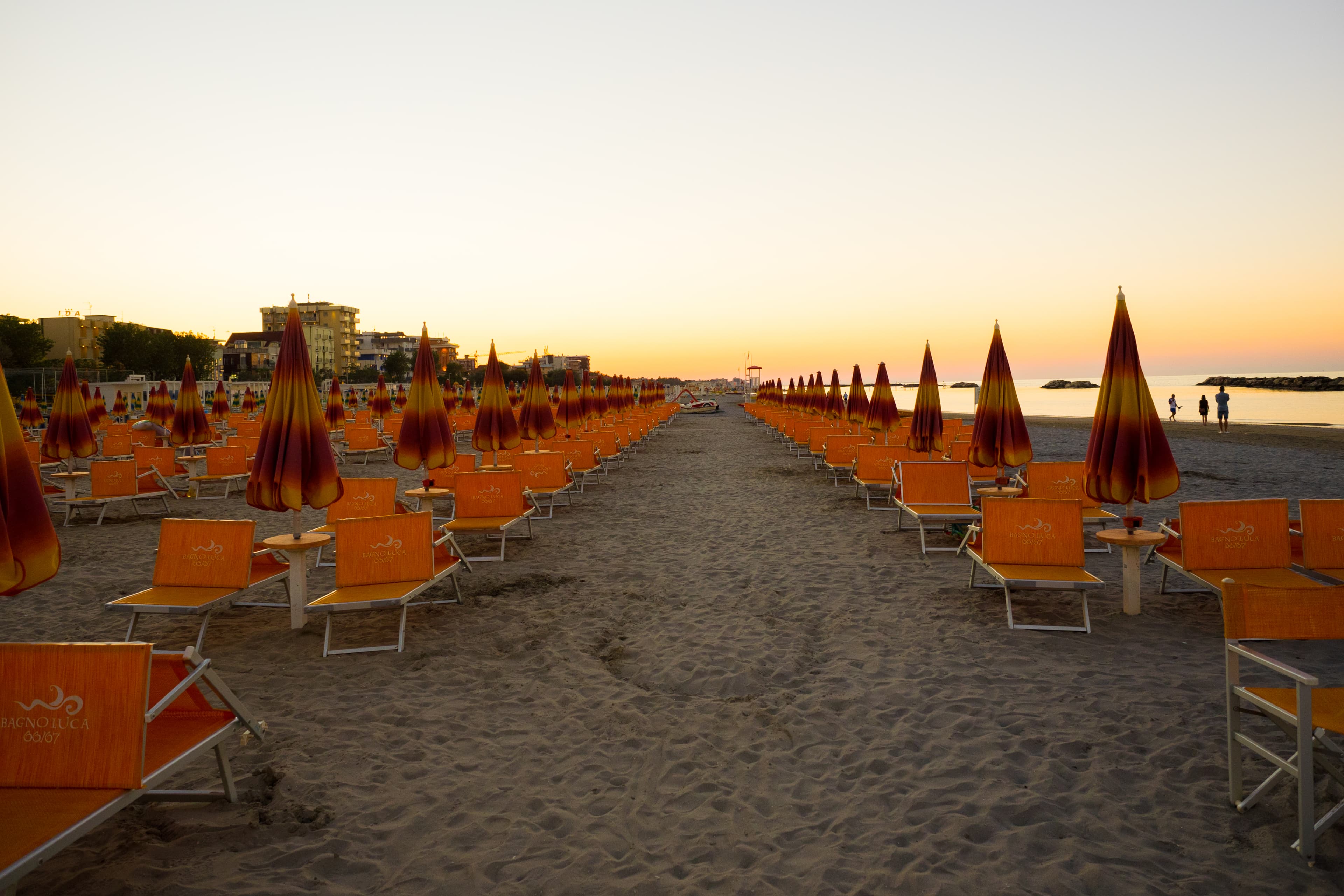 File di ombrelloni chiusi e lettini sulla spiaggia di Rimini al tramonto.