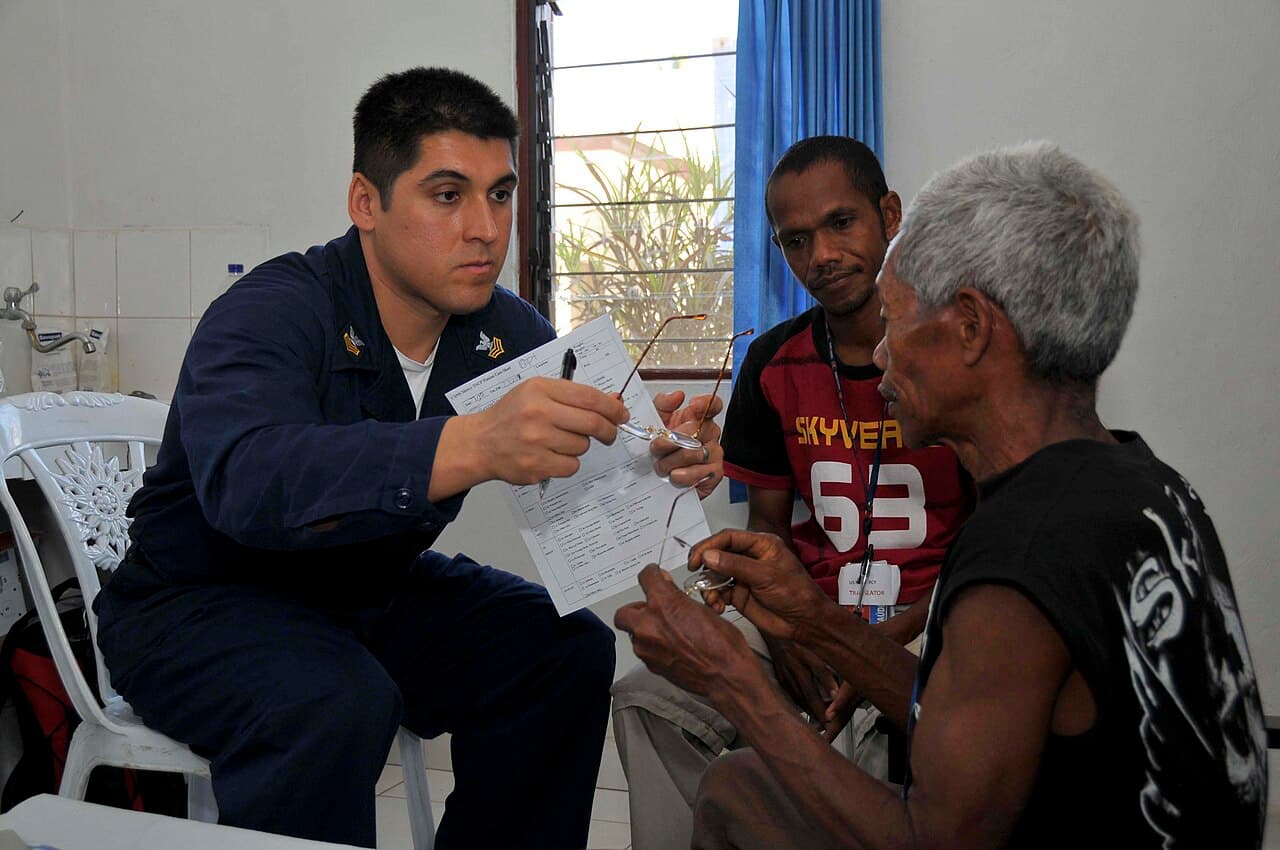 Un operatore sanitario svolge una visita oculistica con un uomo anziano e un interprete.