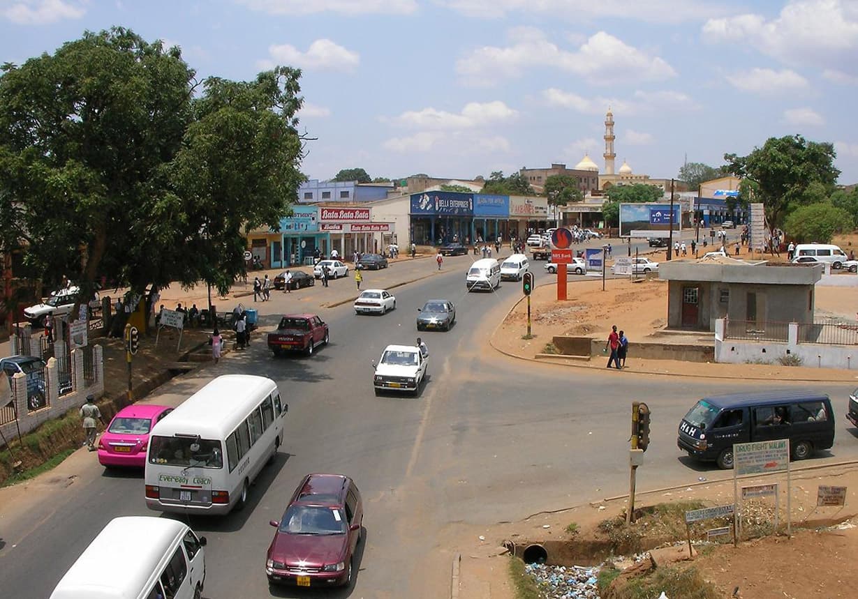Strada dell’Area 2 della città vecchia di Lilongwe, con negozi, alberi e traffico.