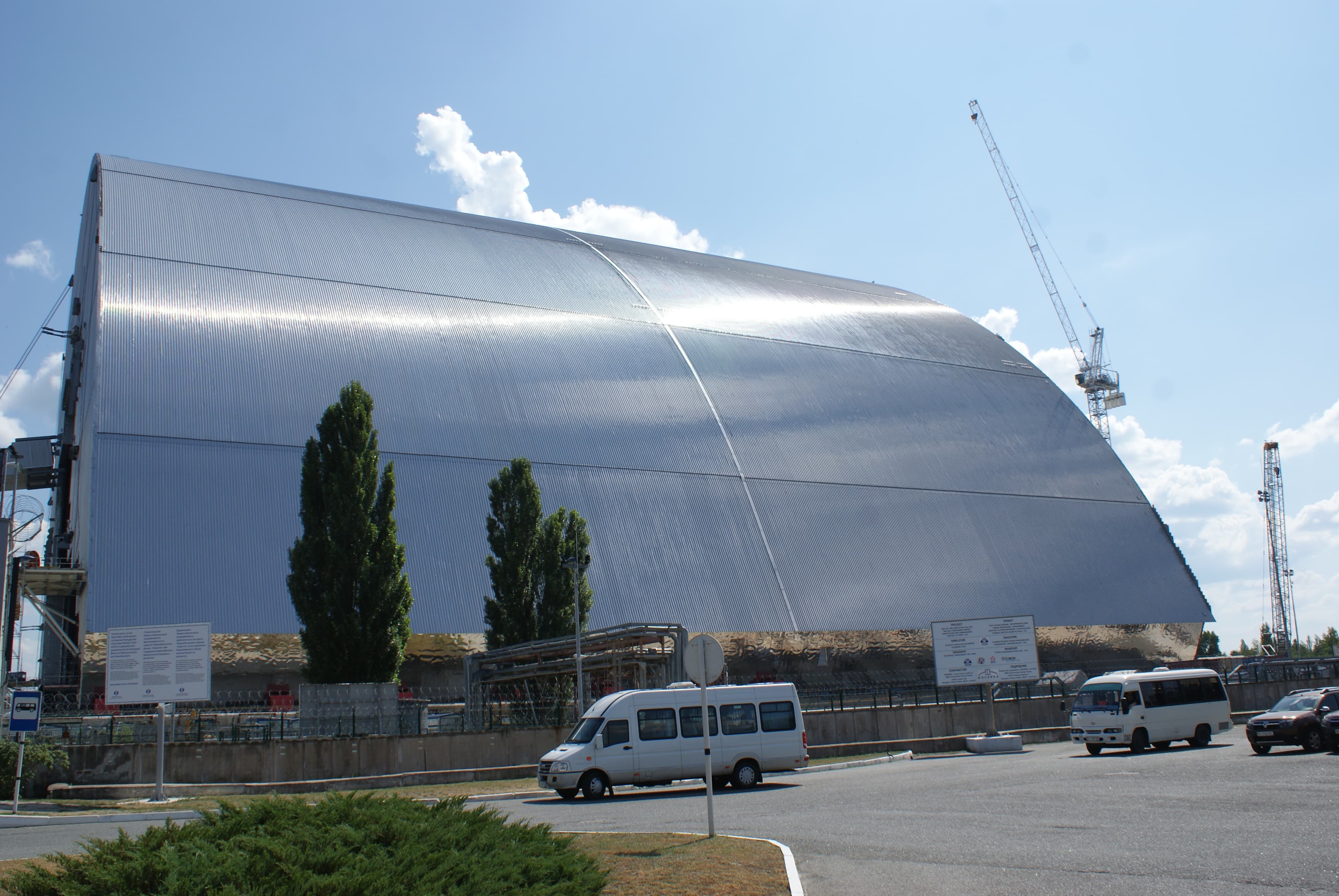 Grande struttura metallica arcuata del New Safe Confinement, con gru al fianco.