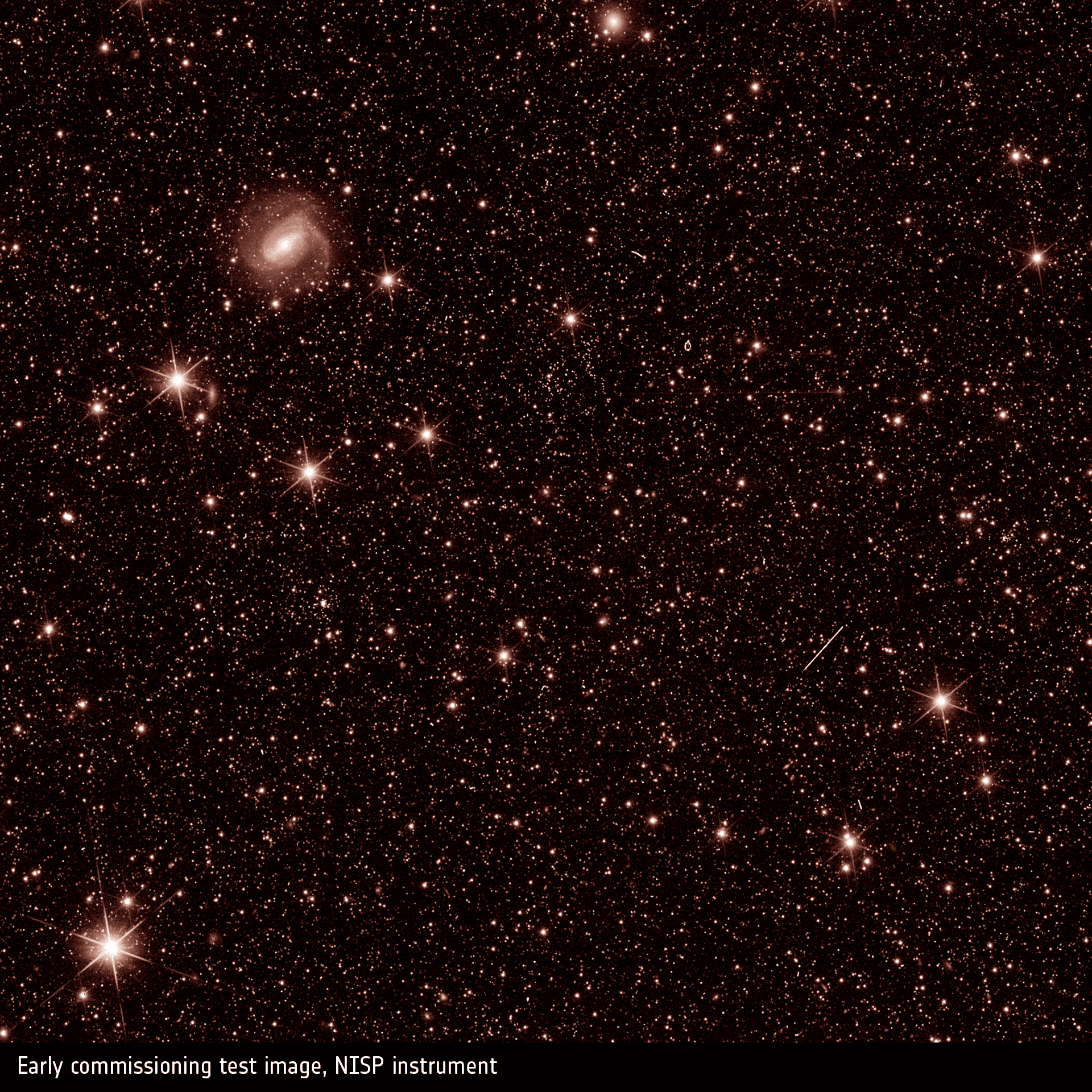 Campo di stelle e galassie dai toni ramati ripreso da NISP, con stelle luminose a punte e una scia obliqua.