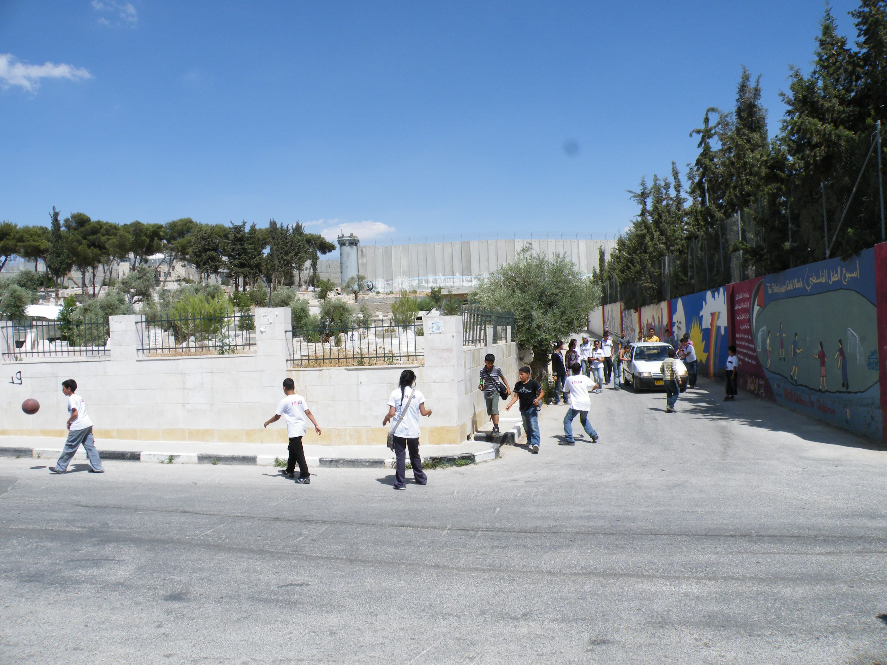 Bambini camminano e giocano in strada vicino al campo di Aida, con un muro sullo sfondo.