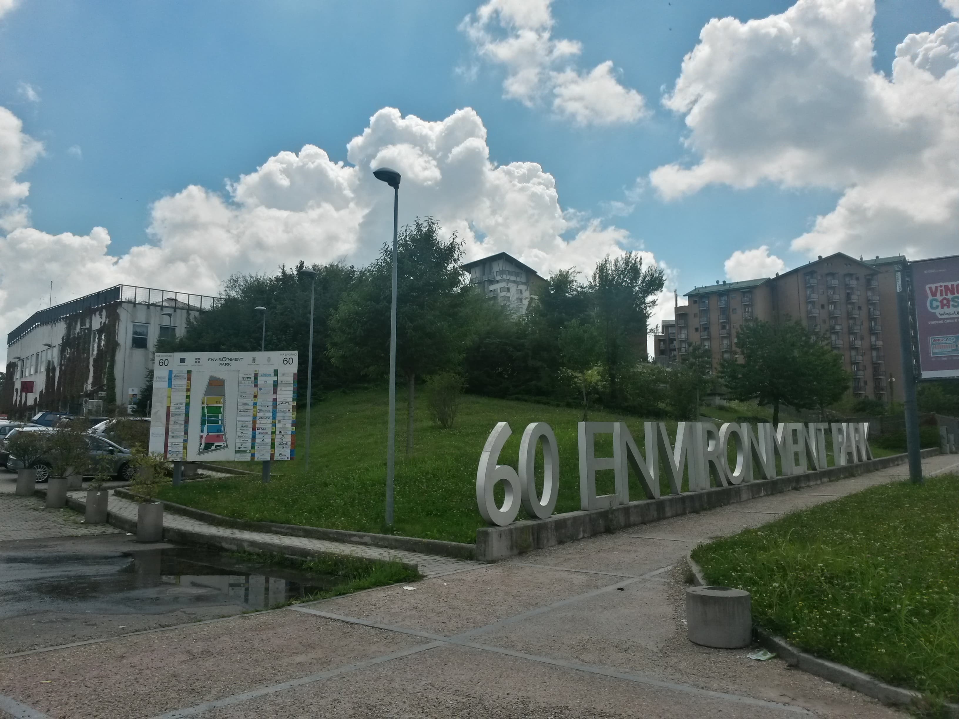 Ingresso dell’Environment Park di Torino con la grande insegna, alberi e prato davanti agli edifici.