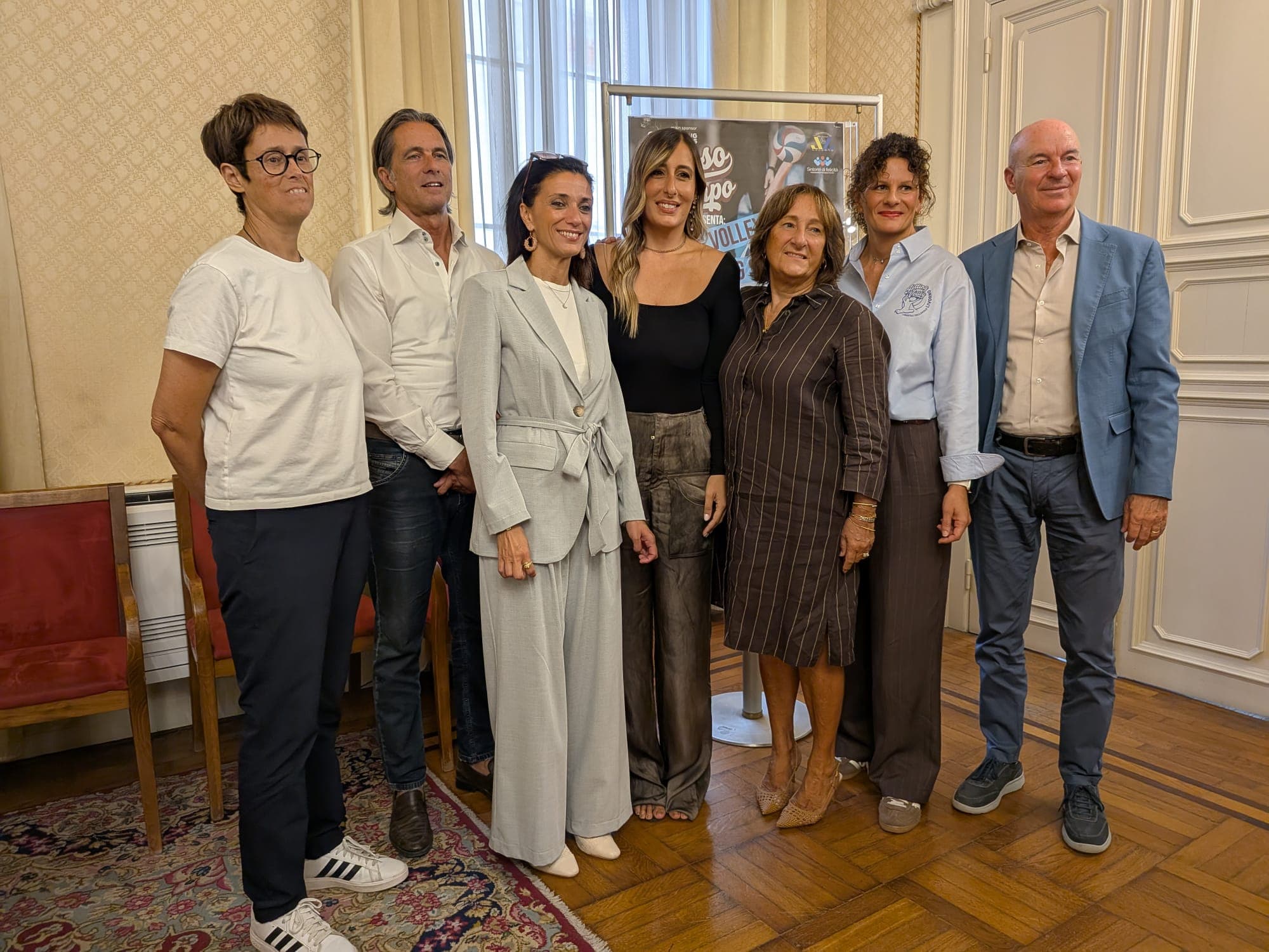 Le persone intervenute alla presentazione di Stesso Campo posano davanti al manifesto del progetto in una sala comunale.