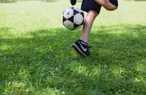 Gambe di un giovane che gioca con un pallone da calcio su un prato.
