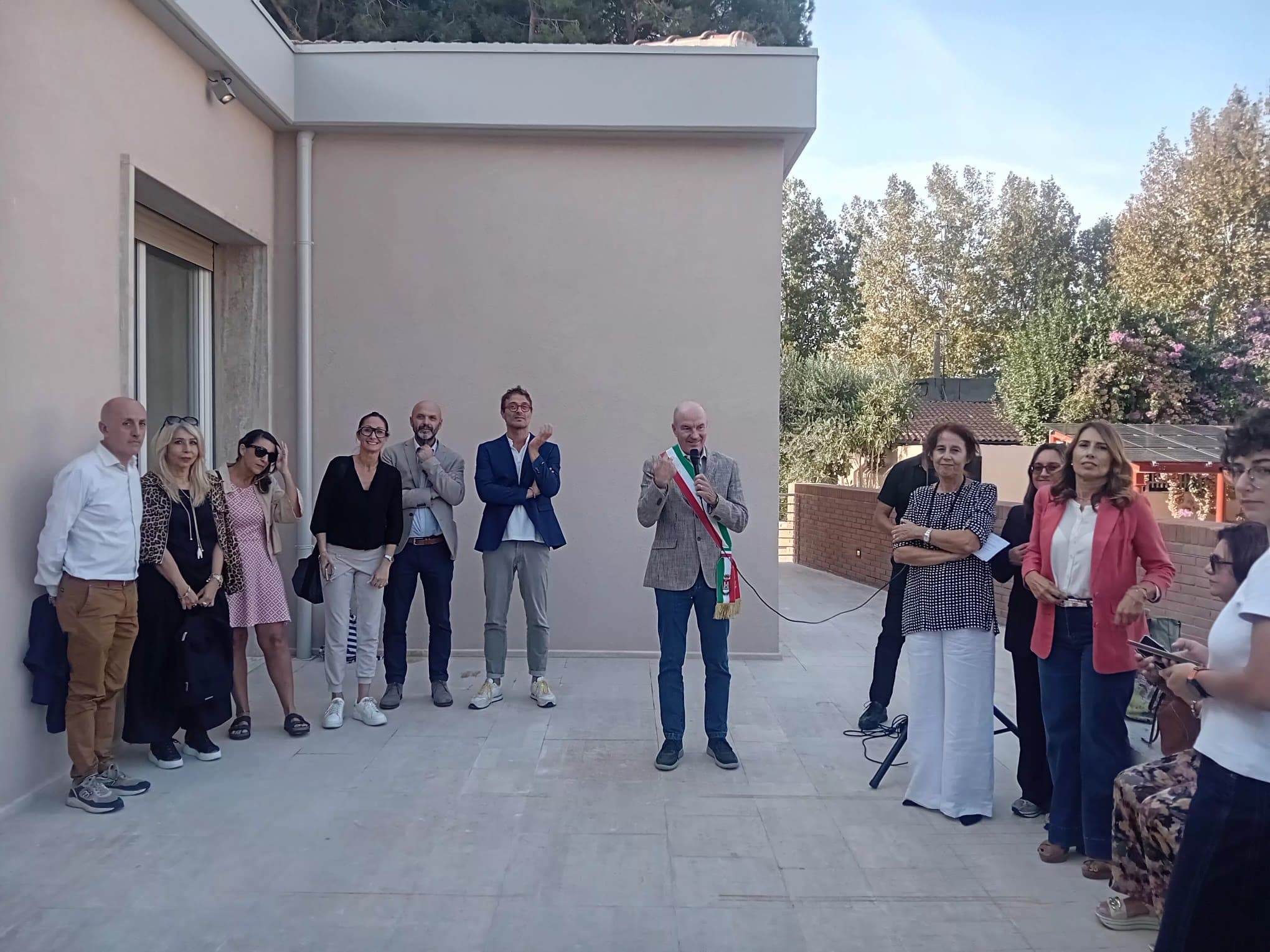 Partecipanti davanti al centro La Trottola durante l’inaugurazione, con un relatore al microfono.
