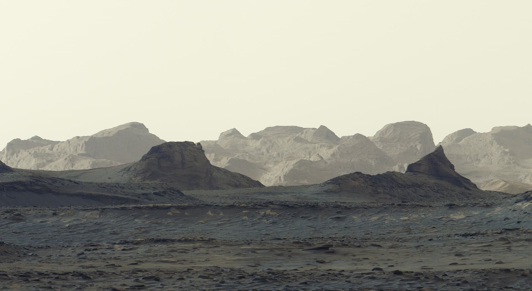 Paesaggio marziano al mattino con rilievi lontani e rocce in primo piano, fotografato da Curiosity.